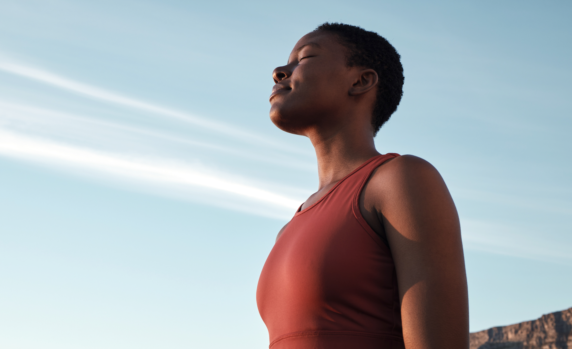 A woman outdoors relaxing and breathing in clean, fresh air with her eyes closed.