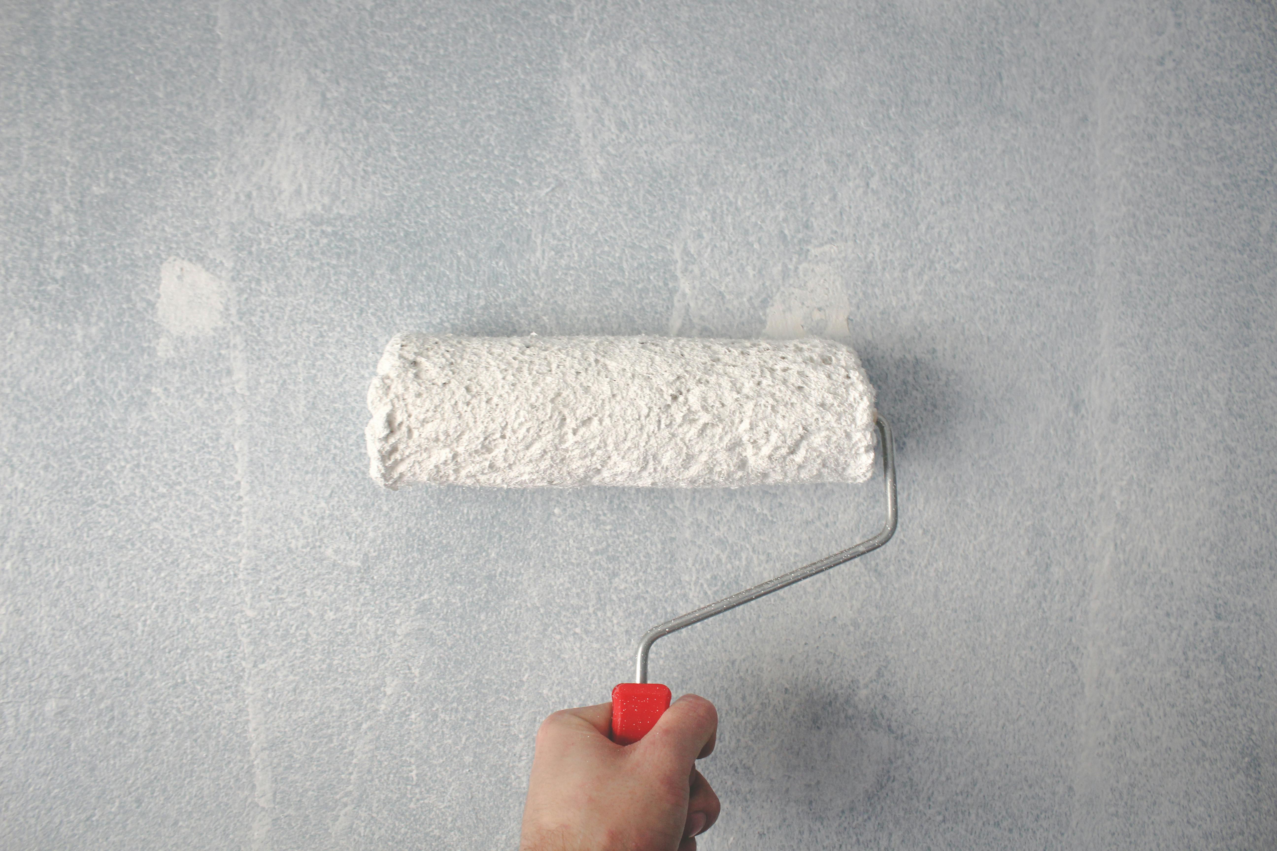 A hand rolling paint onto a wall with a paintbrush, releasing harmful volatile organic compounds into the air.
