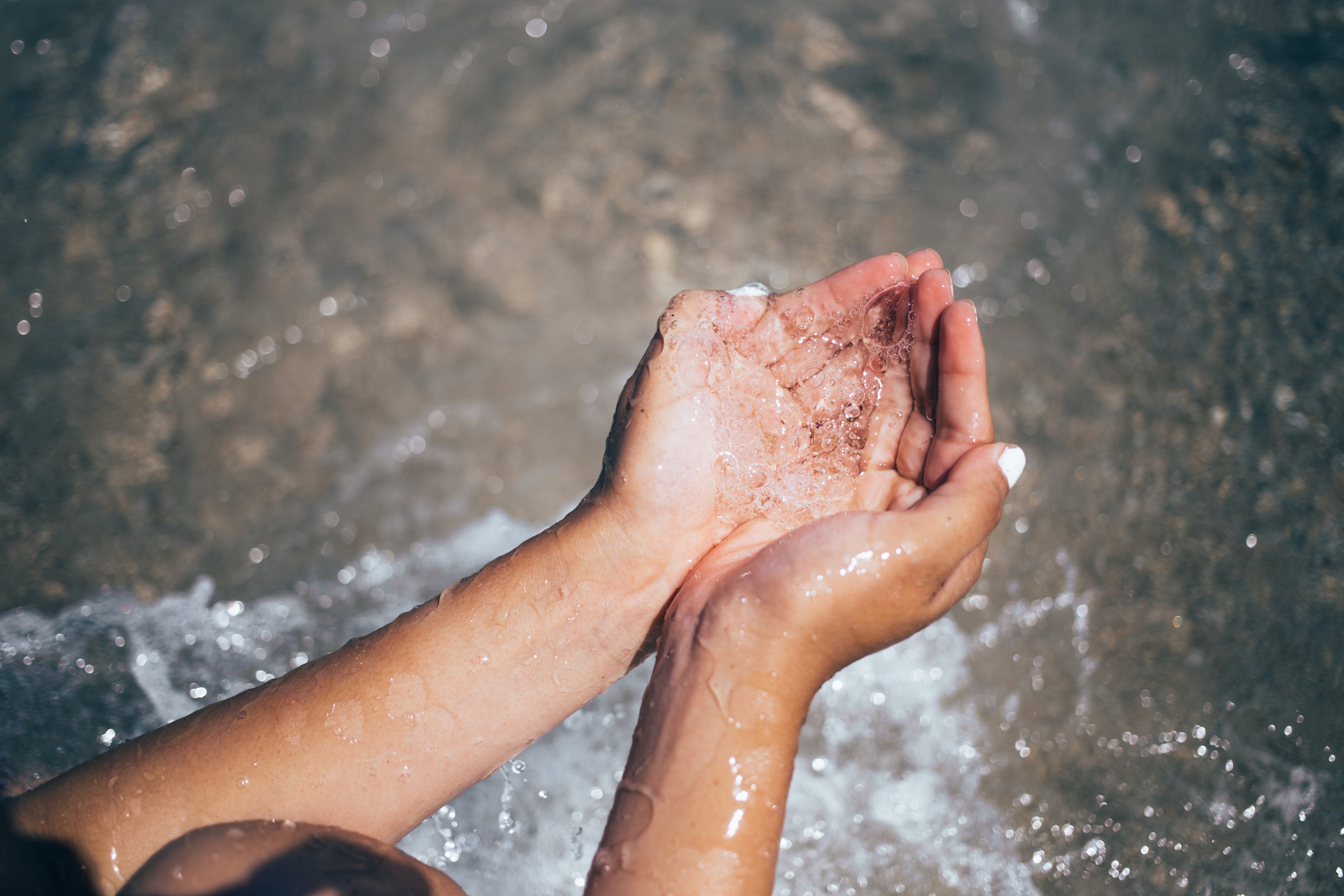 A hand scooping fresh, clean water from a stream.